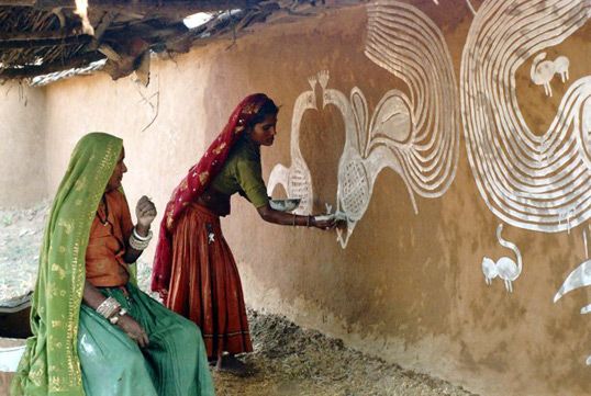 Women in Rajasthan drawing peacocks on the walls.